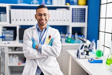 African american man scientist smiling confident sitting with arms crossed gesture at laboratory
