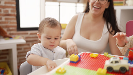 Teacher and preschool student playing with construction blocks sitting on table at kindergarten