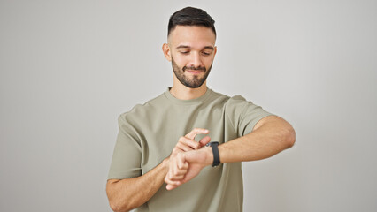 Young hispanic man looking to watch standing over isolated white background