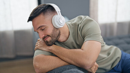 Young hispanic man listening to music sitting on sofa at home