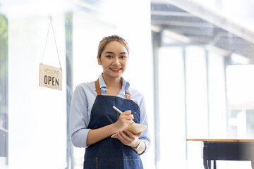 Happy SME business barista cafe owner Asian woman waitress apron and staning at the door with a...