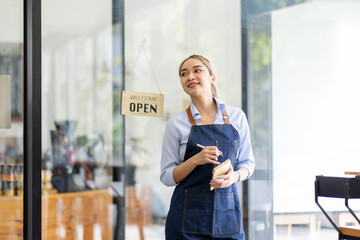 Happy SME business barista cafe owner Asian woman waitress apron and staning at the door with a sign Open waiting for customers , cafes and restaurants entrepreneur Small business concept.