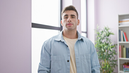 Young hispanic man standing with serious expression at home