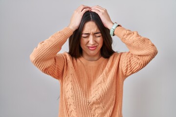 Young brunette woman standing over white background suffering from headache desperate and stressed because pain and migraine. hands on head. - obrazy, fototapety, plakaty