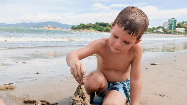 Blonde hair boy playing on seeside. Preschool child build a sand castle.