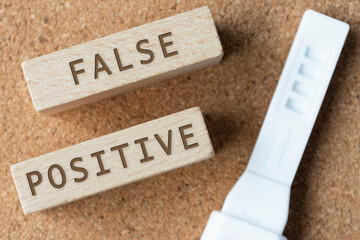 False positive words on wooden block with pregnancy test. - obrazy, fototapety, plakaty