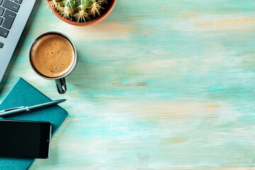 Desk, top view on a wooden blue background. Coffee, notebook, phone, plant, and laptop, overhead flat lay shot. Work layout with a place for text