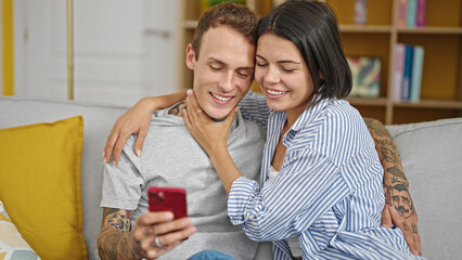 Beautiful couple sitting on sofa together using smartphone smiling at home