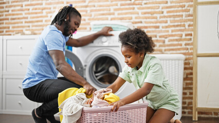 African american father and daughter washing clothes at laundry room