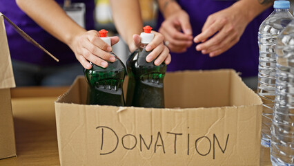 Hands of volunteers putting products on donations cardboard box at charity center