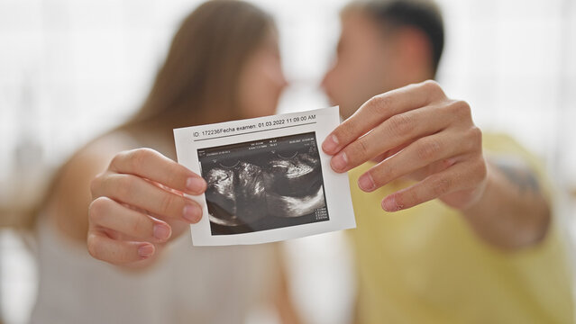 Beautiful couple sitting on bed holding baby ultrasound kissing at bedroom