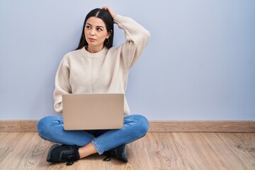 Young woman using laptop sitting on the floor at home confuse and wondering about question....