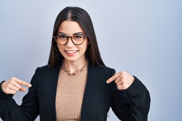 Young brunette woman standing over blue background looking confident with smile on face, pointing oneself with fingers proud and happy.