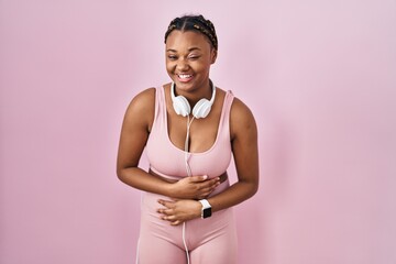 African american woman with braids wearing sportswear and headphones smiling and laughing hard out...
