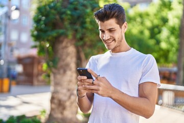 Young hispanic man smiling confident using smartphone at park