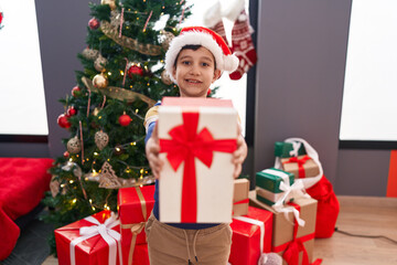 Obraz na płótnie Canvas Adorable hispanic boy holding christmas gift standing at home