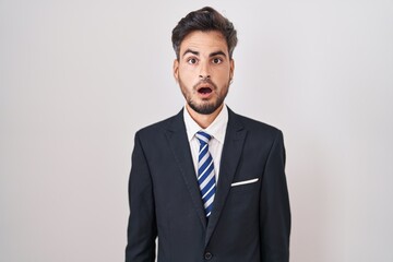 Young hispanic man with tattoos wearing business suit and tie afraid and shocked with surprise and amazed expression, fear and excited face.