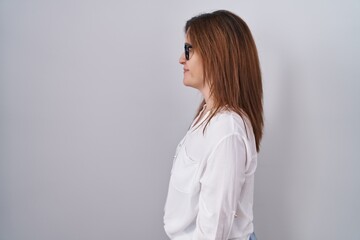 Brunette woman standing over white isolated background looking to side, relax profile pose with natural face and confident smile.