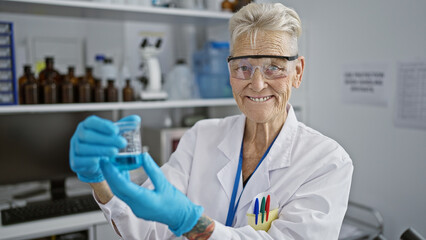 Confident senior grey-haired woman scientist smiling as she works meticulously on a delicate experiment in the bustling lab, test tube in hand