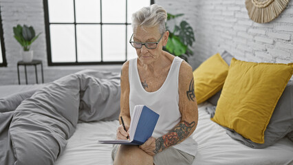 Leisure morning, comfortable, mature woman, relaxing on bed, expressively writing in notebook amidst indoor bedroom setting, short grey-haired elderly probing smart knowledge thrice.