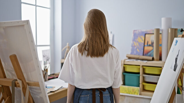 Young blonde woman artist standing backwards at art studio