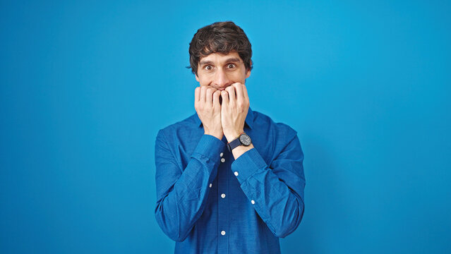Young hispanic man standing with nervous expression over isolated blue background