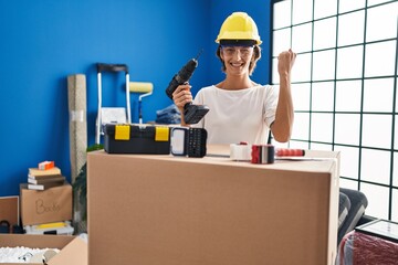 Brunette woman holding screwdriver at new home screaming proud, celebrating victory and success very excited with raised arms