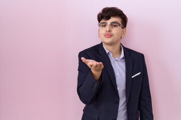 Young non binary man with beard wearing suit and tie looking at the camera blowing a kiss with hand...