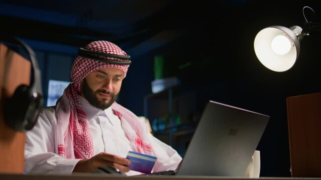 Happy arab man doing internet shopping on computer, spneding money on frivolous things. Smiling Middle Eastern person adding payment method on website in order to purchase products