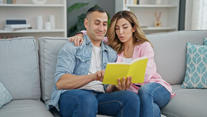Man and woman couple reading book sitting on sof at home