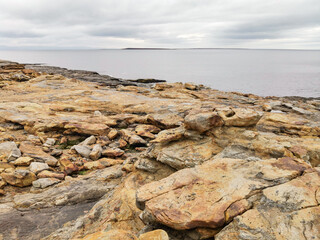 Fototapeta na wymiar The shore of red stones next to the rocks are Two Brothers on the Fishing Peninsula. The picturesque shore of the harsh Barents Sea. The North of Russia. The Kola Peninsula. The Arctic