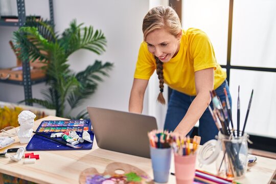 Young blonde woman artist smiling confident using laptop at art studio
