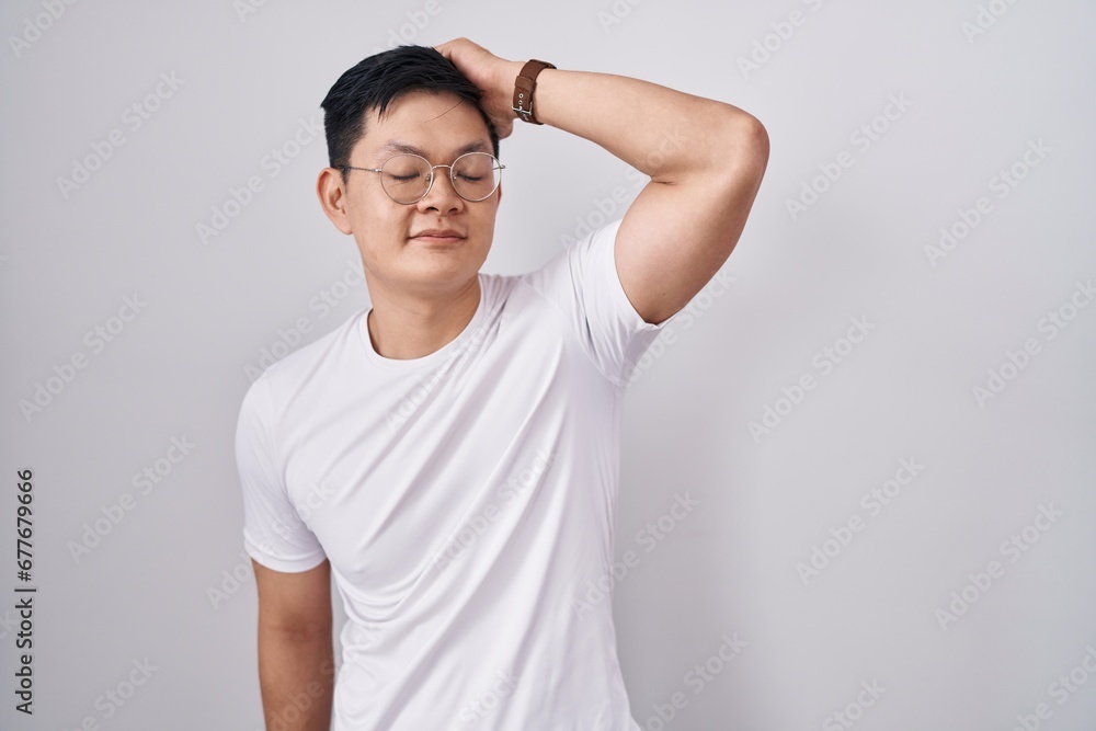 Wall mural young asian man standing over white background smiling confident touching hair with hand up gesture,