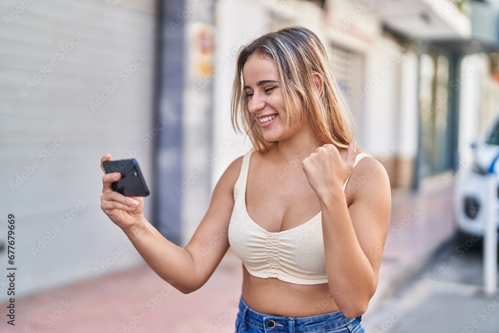 Sticker Young blonde woman smiling confident playing video game at street