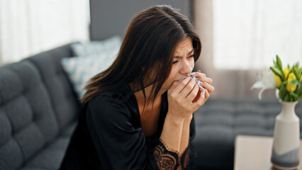 Young caucasian woman wearing dressing gown sitting on sofa stressed at home