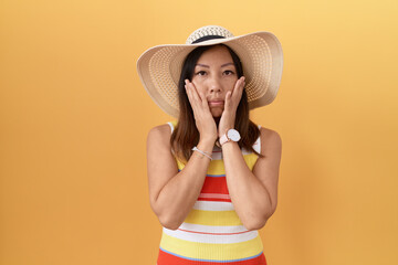 Middle age chinese woman wearing summer hat over yellow background tired hands covering face, depression and sadness, upset and irritated for problem