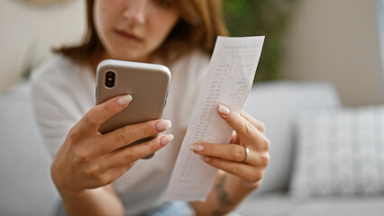 Young woman accounting supermarket ticket with smartphone at home