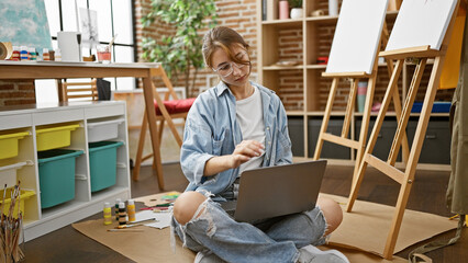 Young woman artist using laptop sitting on floor at art studio