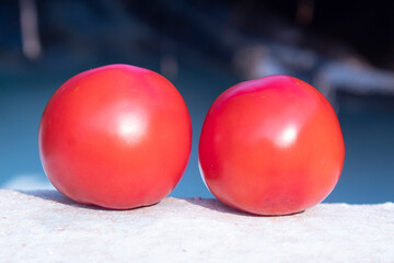 Two red tomatoes on a stone table in front of a blue background
