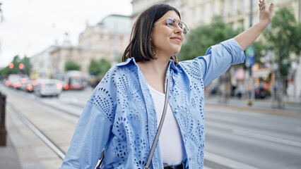 Young beautiful hispanic woman calling for taxi with hand raised in the streets of Vienna