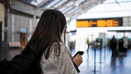 Young beautiful hispanic woman looking at train schedule on smartphone at train station