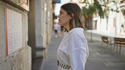Young beautiful hispanic woman reading restaurant menu at the street