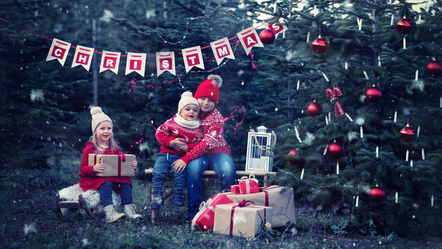drei kleine Kinder sitzen am Weihnachtsbaum