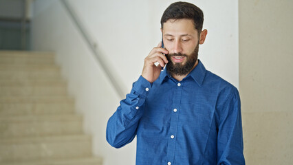 Young hispanic man business worker talking on smartphone smiling at the office