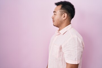 Chinese young man standing over pink background looking to side, relax profile pose with natural face and confident smile.