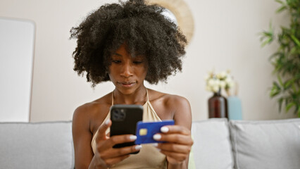 African american woman shopping with smartphone and credit card sitting on sofa at home