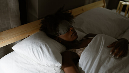 African american woman wearing sleep mask lying on bed sleeping at bedroom