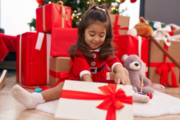 Adorable hispanic girl unpacking gift sitting by christmas tree at home