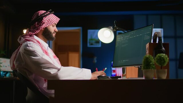 Smiling muslim engineer writing script code on computer screen using Java programming languages. Self employed Middle Eastern developer at home working on fixing database errors