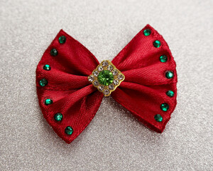 on a silver background lies a burgundy bow with shiny white to green stones in the middle....